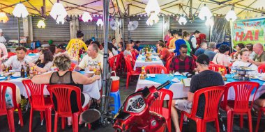 Ho Chi Minh City, Vietnam - 1 Mayıs 2018: Gezginler Ben Thanh Market 'teki bir sokak yemeği restoranının barakasının altındaki kırmızı plastik sandalyelerde otururlar..