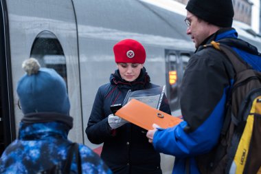Saint Petersburg, Rusya - 29 Ekim 2017: Sapsan ekspres tren kırmızı bereli bir kondüktör Moskovsky tren istasyonunda çocuklu bir yolcuyu elektronik cihaz kullanarak kontrol ediyor..