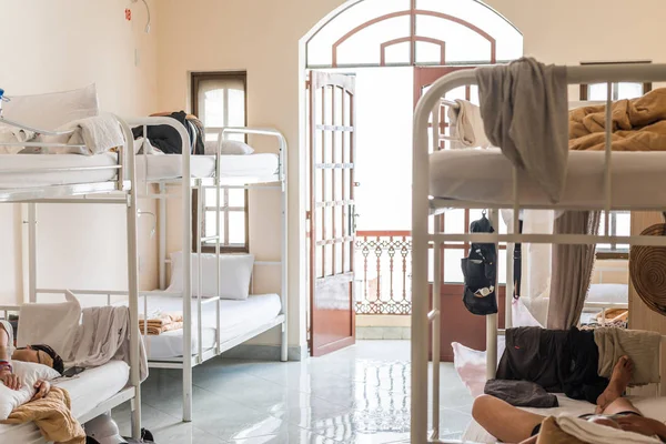 Hostel dormitory with bunk beds and sleeping travelers. Real hostel\'s interior with some mess.