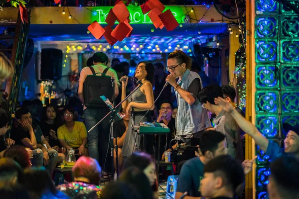 Ho Chi Minh City, Vietnam - 29 Nisan 2018: Gülümseyen bir kadın kalabalıkla çevrili bir müzik grubuna eşlik etmek için mikrofonla şarkı söylüyor, bir kısmı dışarıda Bui Vien Caddesi 'nde yürüyor..