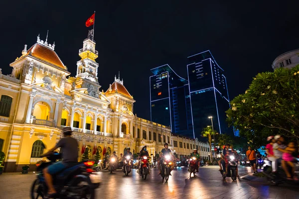 Ho Chi Minh Şehri, Vietnam - 1 Mayıs 2018: Saigon Belediye Binası, Vincom Merkezi kuleleri, renkli sokak trafiği ve gece gökyüzüne karşı tropikal bitkiler. Saygon şehir merkezi gece hayatı ve ünlü simgeler