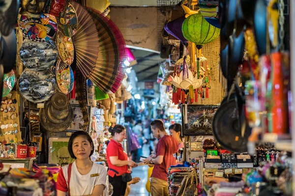 Ho Chi Minh City, Vietnam - 27 Nisan 2018: Genç gülümseyen kadın satıcı rafların arasında rafların arasında Ben Thanh Market 'in bir geçidinde oturuyor (kağıt el hayranları ve fenerler, Breaking Bad serisinin bir posteri, vb.).