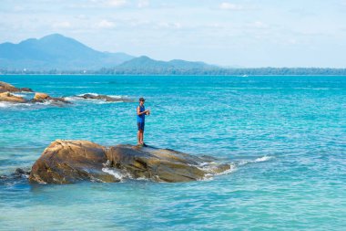 Ko Samet, Tayland - 31 Aralık 2017: Tayland Körfezi 'nin deniz mavisi sularında bulunan bir kayanın üzerinde dönen bir adam balık tutar. Balık turizmi Tayland 'da daha popüler hale geliyor.