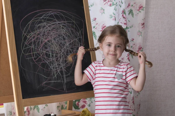 El niño está dibujando con trozos de tiza de color en la pizarra. Chica está expresando creatividad y mirando a la cámara. Concepto de expresión y aprendizaje — Foto de Stock