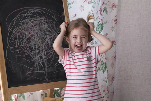 El niño está dibujando con trozos de tiza de color en la pizarra. Chica está expresando creatividad y mirando a la cámara, sala de juegos sonriente. Concepto de expresión y aprendizaje — Foto de Stock