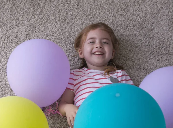 Flicka med ballonger, barn med ballonger, barn med ballonger liggande på golvet. Flickan är att uttrycka kreativitet och tittar på kameran och leende. — Stockfoto