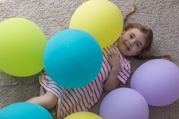 Niña con globos, niño con globos, niño con globos tumbados en el suelo. Chica está expresando creatividad y mirando a la cámara y sonriendo . — Foto de Stock