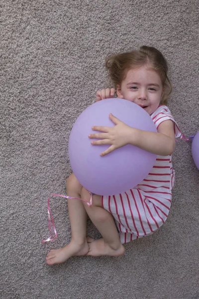 Flicka med ballonger, barn med ballonger, barn med ballonger liggande på golvet. Flickan är att uttrycka kreativitet och tittar på kameran och leende. — Stockfoto