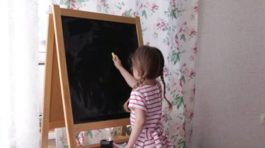 Blackboard küçük okul öncesi kız yazma harfler. Tebeşir tutarak ve çizim yürümeye başlayan çocuk kız.