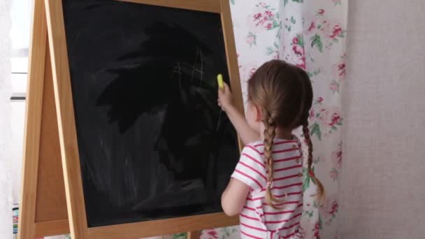 Pequeña niña preescolar escribiendo cartas en pizarra. Niña sosteniendo tiza y dibujo . — Vídeos de Stock
