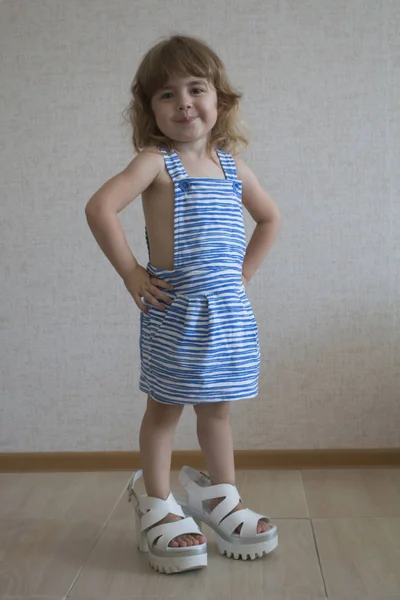 Liten modell poserar i studio. Liten modell med lång hår. Hon står i hennes mödrar stora skor och tittar på kameran. — Stockfoto