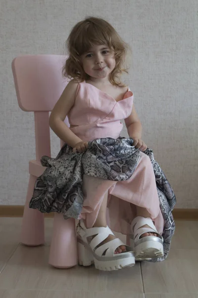 Niña divertida sentada en una silla en sus madres zapatos grandes y vestido — Foto de Stock