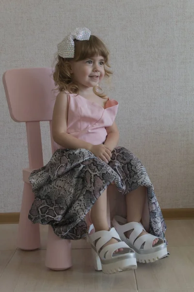 Niña divertida sentada en una silla en sus madres zapatos grandes y vestido — Foto de Stock