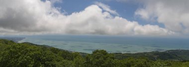 Deniz üzerinde bulutlar. Öndeki yeşil dağlar. panorama