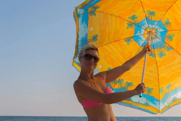 Glimlachende vrouw in een zonnebril tegen een blauwe lucht houdt een grote parasol in zijn handen — Stockfoto