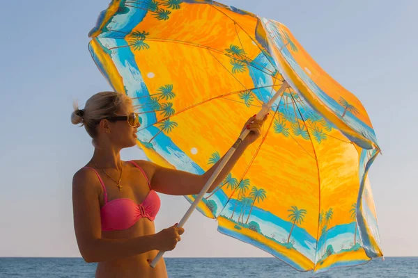 Glimlachende vrouw in zonnebril en bikini aan zee onder een paraplu in de zomer — Stockfoto