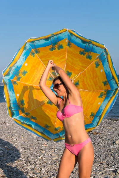 Yazın deniz kenarında güneş gözlüklü ve bikinili gülümseyen kadın şemsiyenin altında.