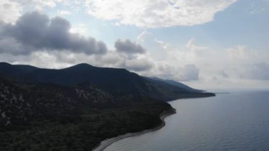İHA 'dan ateş edilmiş. Deniz kenarındaki çam ormanlarıyla kaplı güzel dağlar. Dağların üzerinde fırtına bulutları. 4k