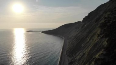 Hava sineması: Gün batımında deniz kıyısında uçan bir dron. Drone denizin üzerinde uçuyor. Güzel bir deniz manzarası. Kayaların üst görüntüsü