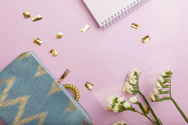 beyaz çiçekler, konfeti ve mor zemin üzerine mavi kozmetik çantası. Üstten görünüm, düz yatıyordu. Metin için yer.