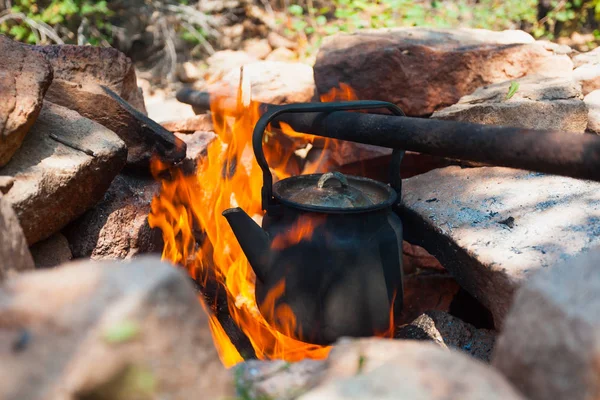 Boiling of tea in kettle on bonfire with large firewood. Tea drinking in open air. Active outdoor recreation. Camping in dusk. Romantic warm atmosphere in twilight on nature. Active rest.