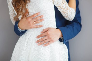 Bel bir örtü ile işlemeli beyaz giysili bir gelin hugs mavi elbiseli damadın Close-up eller.