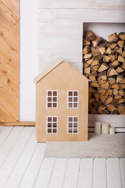 Bej oyuncak ev ahşap ve beyaz bir duvar ile bir woodpile arka planda. Rahat rustik iç. Dekoratörler, stüdyo için dekorasyon fikirleri