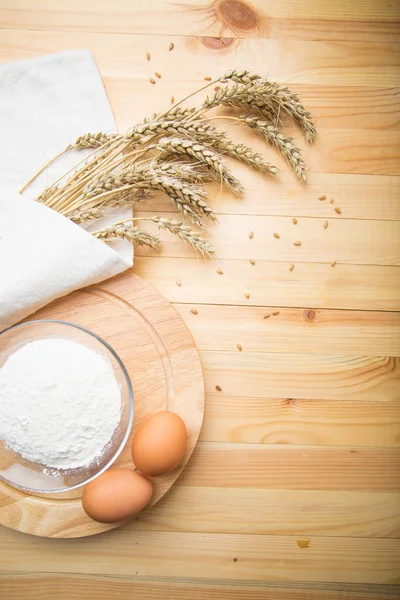 小麦的卵和耳朵躺在白色帆布上 旁边一碗面粉在圆形木架上 在光明背景下的农业静物 图库图片