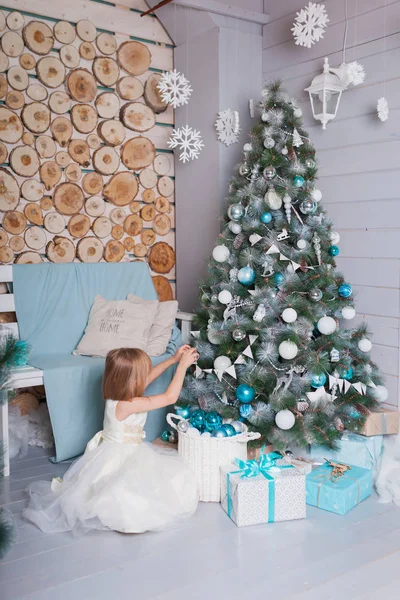 美丽的孩子穿着白色的衣服装饰圣诞树 打开礼物 图库照片