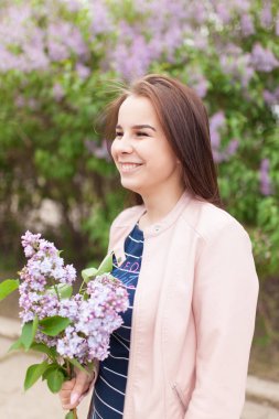 Genç güzel kız çiçek açan Lila çalıların yakınında duruyor
