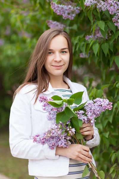 Молодая красивая девушка стоит рядом с кустами цветущей сирени — стоковое фото