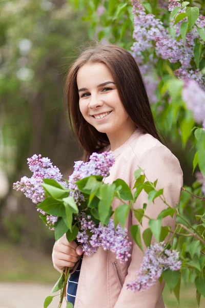 Fiatal gyönyörű lány áll, közel a bokrok a virágzó lila — Stock Fotó