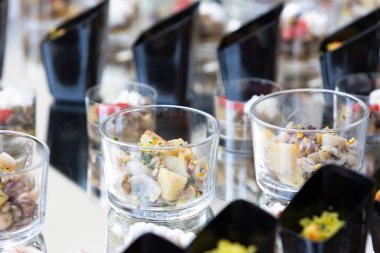 Mürekkep balığı ve patates salatası içeren küçük cam bardaklar aynalı bir yüzeye dizilir ve sofistike bir yemek servisi sunumu sergilenir.