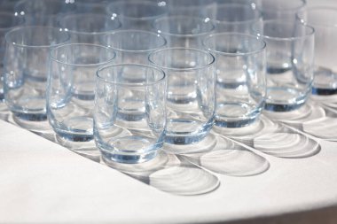 Sıralar dolusu boş, berrak içki bardakları beyaz bir masa örtüsünde kullanılmaya hazır, parlak güneş ışığında ilginç gölgeler bırakıyor.