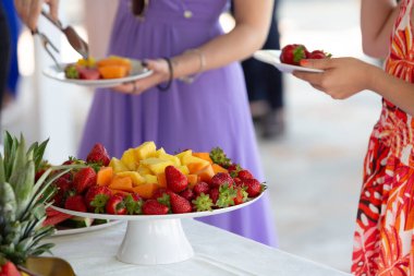 Guests are taking fresh fruit from a buffet table, enjoying a healthy and refreshing snack