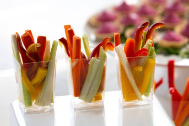 Havuç, kereviz ve dolma biber içeren taze sebze aperatifleri açık büfe masasında plastik bardaklarda sunuluyor.