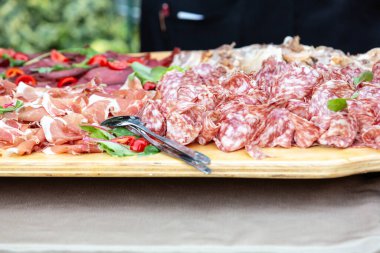 Wooden charcuterie board laden with various cured meats, prosciutto, salami, and garnishes, ready for serving at a catered event
