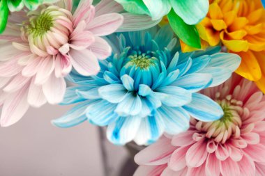 Ortasında mavi bir çiçek olan bir buket çiçek. Diğer çiçekler pembe, sarı ve beyazdır. Buket bir vazoya yerleştirildi.