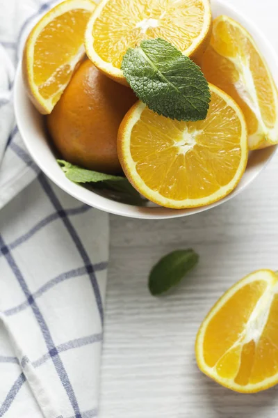 oranges in a white cup and mint leaves on a white wooden background closeu