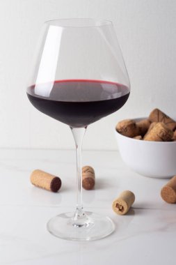 bir bardak beyaz zemin üzerine kırmızı şarap ve şarap mantarlar