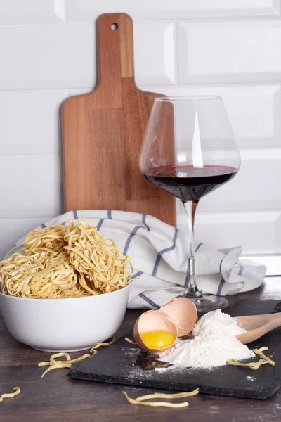 broken egg, flour and egg noodles and a glass of wine on a white background