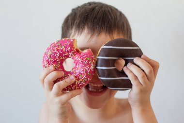 Neşeli çocuk elinde çikolatayla donut tutuyor.