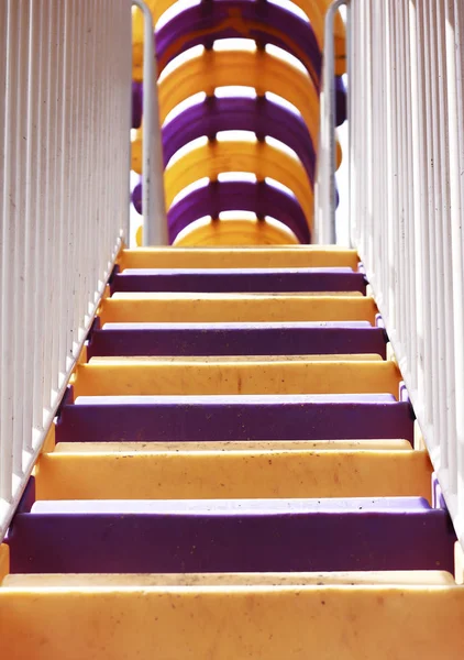 Colorful violet and yellow plastic stairs with white metal railing going up.