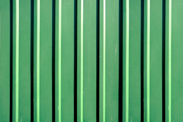 Green, crumpled, crimson metal sheet wall fence for industrial building and construction. Abstract green metal door texture background close up.
