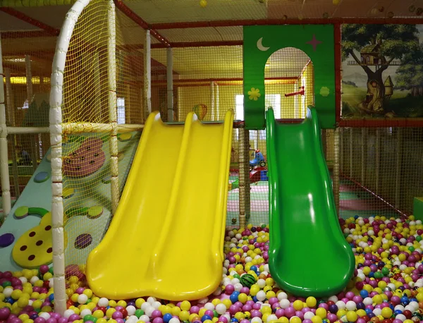 黄色和绿色的婴儿滑梯下降到游泳池与许多彩色球在孩子们的游戏室 — 图库照片