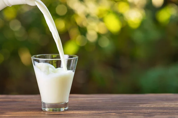 Milk from jug pouring into glass — Stock Photo, Image