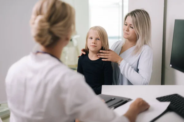 Mom with kid girl with blond hair at doctor in pediatrician appointment.