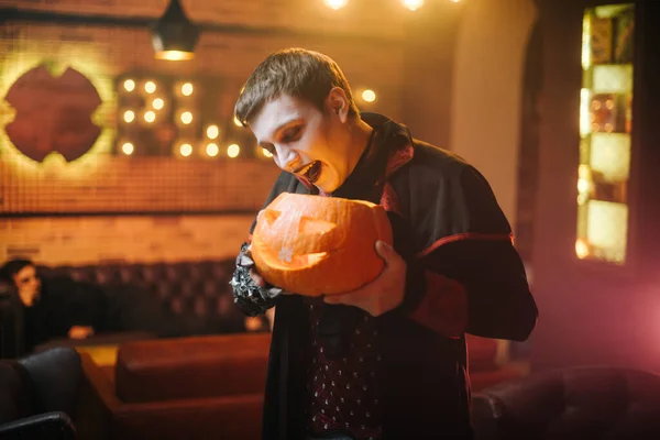 Guy in a Halloween costume of Count Dracula holds a carved festive pumpkin