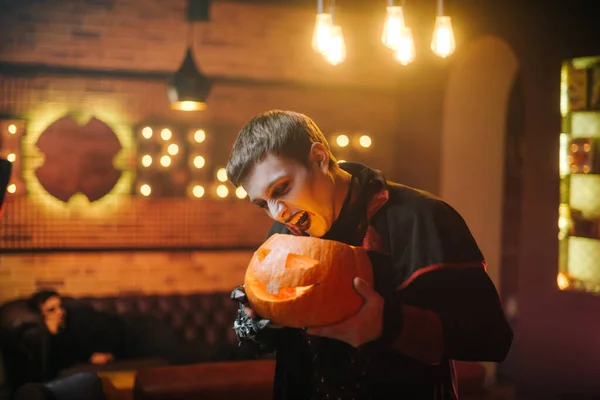 Young man in a Halloween costume of Count Dracula holds a carved festive pumpkin