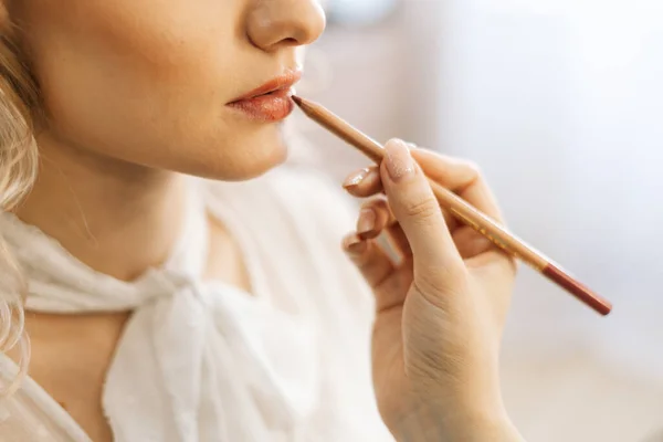 Close-up of professional make-up artist making makeup young woman lips with lip pencil